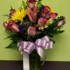 Bouquet of pink roses and yellow lilies in a glass vase with a lavender ribbon