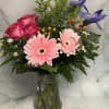 Pink roses and gerbera daisies in a clear glass vase with purple irises