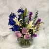 Mixed bouquet in a clear glass vase with blue, white, pink, and purple flowers