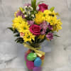 Bouquet of yellow daisies, pink roses, and lilies in a glass vase with colorful eggs