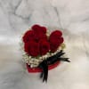 Red roses arranged in a heart-shaped box with white filler flowers and a black ribbon