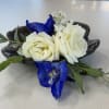 Small floral corsage with white roses and blue flowers on a dark base