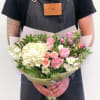 Handheld bouquet of pink and white flowers wrapped in pale paper