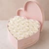 Tightly packed garden-white roses nestle inside a pale pink heart-shaped box edged