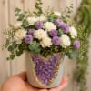 Small bouquet of white and lavender flowers in a decorated pot