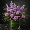 Lavender roses and purple flowers arranged in a glass vase