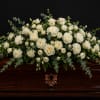 A wide, low casket spray of white roses and clustered white carnations
