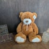 Brown teddy bear with a ribbon sitting beside a glass candle holder