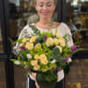 Woman holding a bouquet of pale yellow roses and purple tulips in a glass vase