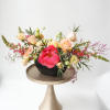 Mixed bouquet of peach and pink flowers in a black bowl on a pedestal stand
