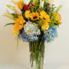 Mixed bouquet in a clear glass vase with sunflowers, roses, lilies, and hydrangeas