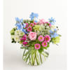 Mixed bouquet of pink roses, blue flowers, and daisies in a clear glass vase