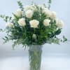 White roses arranged in a clear glass vase with greenery