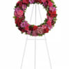 Circular floral wreath on a white easel with red, pink, and purple blooms