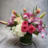 Pink lilies and roses arranged in a glass vase with white hydrangea.