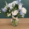 White roses and blue flowers arranged in a glass vase