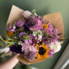 Handheld bouquet of pink, purple, white, and yellow flowers wrapped in brown paper