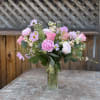 An arrangement of peonies, roses, in season flowers and greenery. In glass