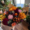 Handheld bouquet of mixed orange, pink, and burgundy flowers in brown paper