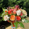 Mixed bouquet of orange, peach, and white flowers in a clear glass vase on a wooden railing