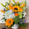 Bright arrangement of sunflowers, orange roses, lilies and hydrangeas in a white cylinder vase