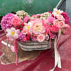 Pink floral arrangement in a woven basket with ribbon accents