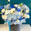 Blue and white floral arrangement in a gray hatbox with ribbon