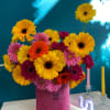 Bright gerbera daisy arrangement in a pink hatbox with candles nearby