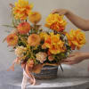 Basket arrangement of yellow-orange roses and peach pompon flowers