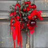 Holiday wreath with red ornaments and ribbon on a gray door