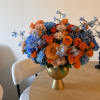 Colorful bouquet of orange, blue, and peach flowers in a gold vase