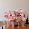 Pink floral arrangement in a textured bowl with cascading bead strands