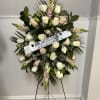 Standing floral wreath of white and blush roses on an easel with a ribbon