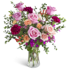 Tall arrangement of pink roses, peach carnations, and magenta blooms in a clear glass vase