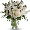 White lilies, roses, and hydrangeas arranged in a clear glass vase.