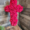 Standing cross of hot pink roses on a metal easel against a wood wall.