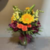 Mixed bouquet with orange roses, yellow daisies, and purple flowers in a glass vase