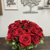 Two dozen red roses in a low, clear vase with greenery.
