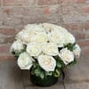 Two dozen white roses in a low, clear vase with greenery.