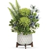 Green floral arrangement in a white ceramic pot on a wooden stand