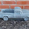 Gray pickup truck-shaped planter on mulch in front of a brick wall