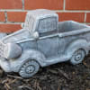 Gray pickup truck-shaped planter on mulch in front of a brick wall