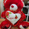 Red teddy bear holding a white heart with the word love