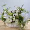 Low white arrangement with orchids, anemones, calla lilies, and hydrangeas in a white ceramic vase