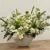White and green flower arrangement in a textured white bowl on a wooden surface