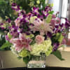 Pink lilies, roses, hydrangeas, and purple orchids in a clear glass vase