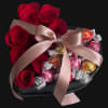 Red roses arranged with wrapped chocolates in a black box, tied with a pink ribbon.