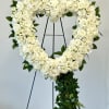 Heart-shaped white floral wreath on a stand with trailing ivy