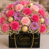Pink and purple flower arrangement in a black gift box with gold chocolates