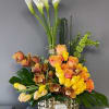 Tall floral arrangement with white calla lilies, roses, and orchids in a gold vase